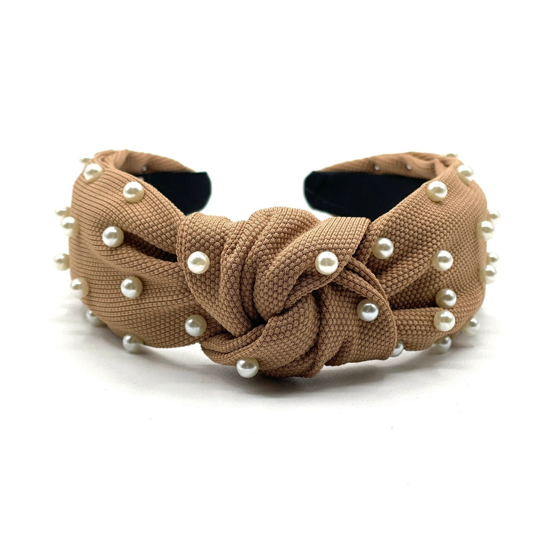 A brown knot headband with white pearls embellished on a textured fabric.