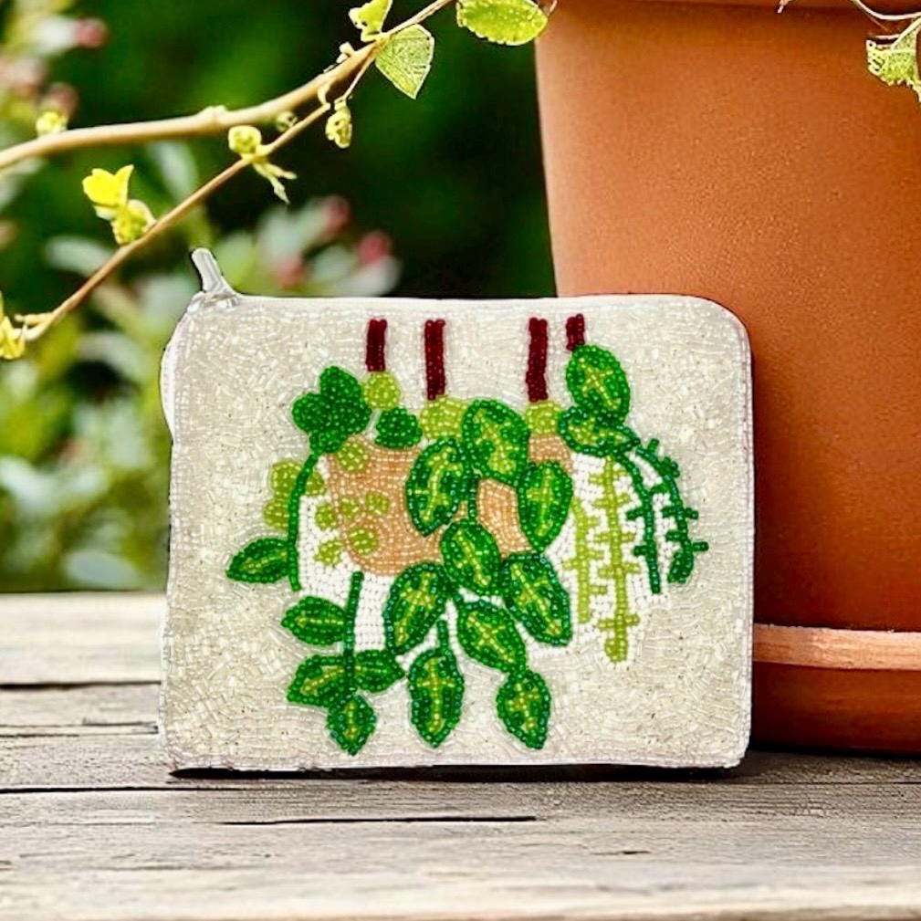 Small pouch with green leaf design on a wooden surface with a plant in the background