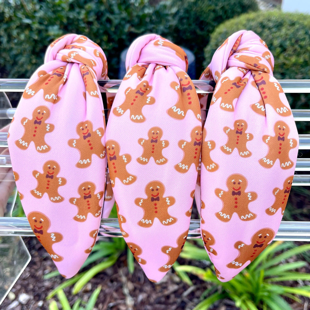 Three hair ties with gingerbread man pattern on a metal rack with greenery in the background.