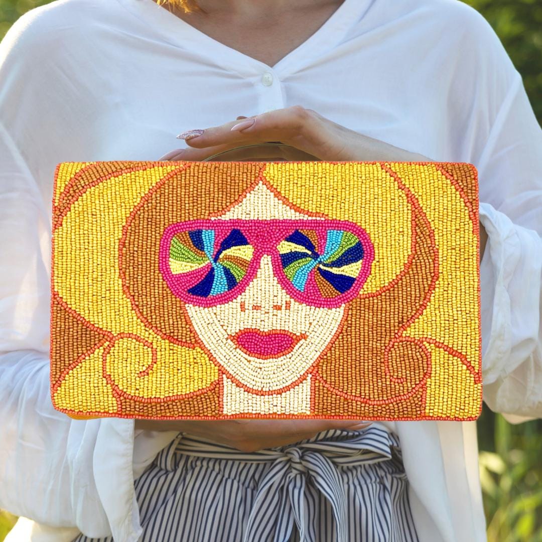 Person holding a colorful beaded clutch with a face design and sunglasses.
