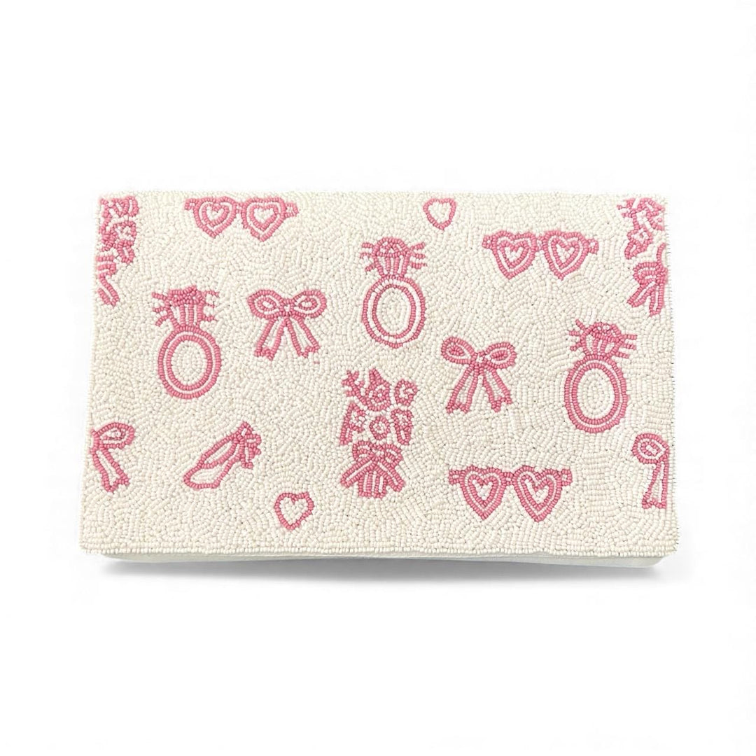 Beige clutch with pink heart, bow, and ring patterns on a white background