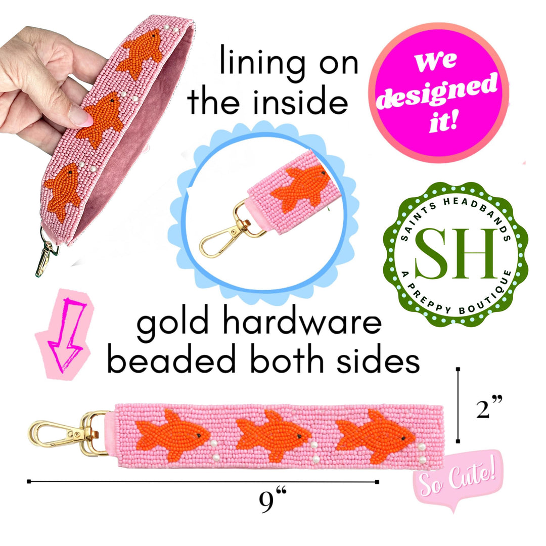 Pink beaded strap with gold hardware and orange fish design, held by a hand.