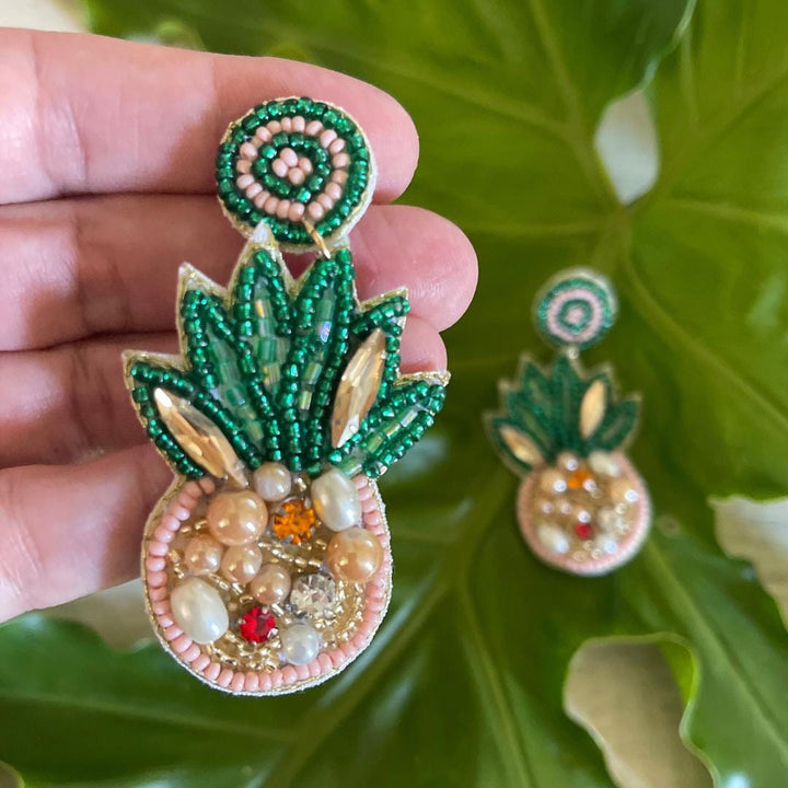 Decorative earrings with green and gold beading on a leafy background