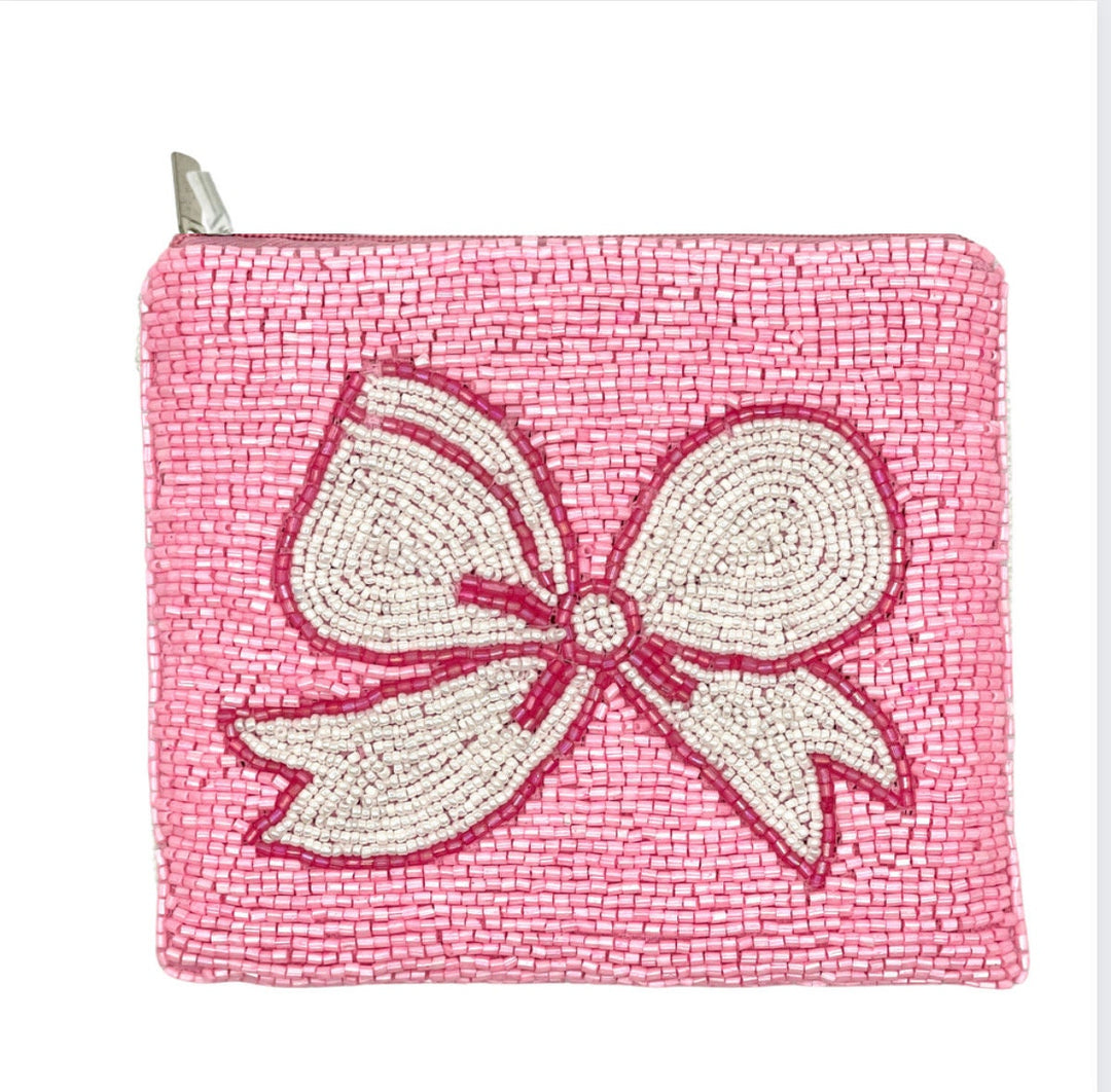 A small, pink beaded coin purse with a white bow design and a zipper closure, featuring a canvas backing.